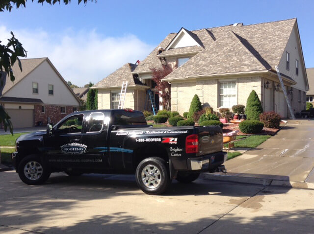 black truck in front of house getting new roof installed