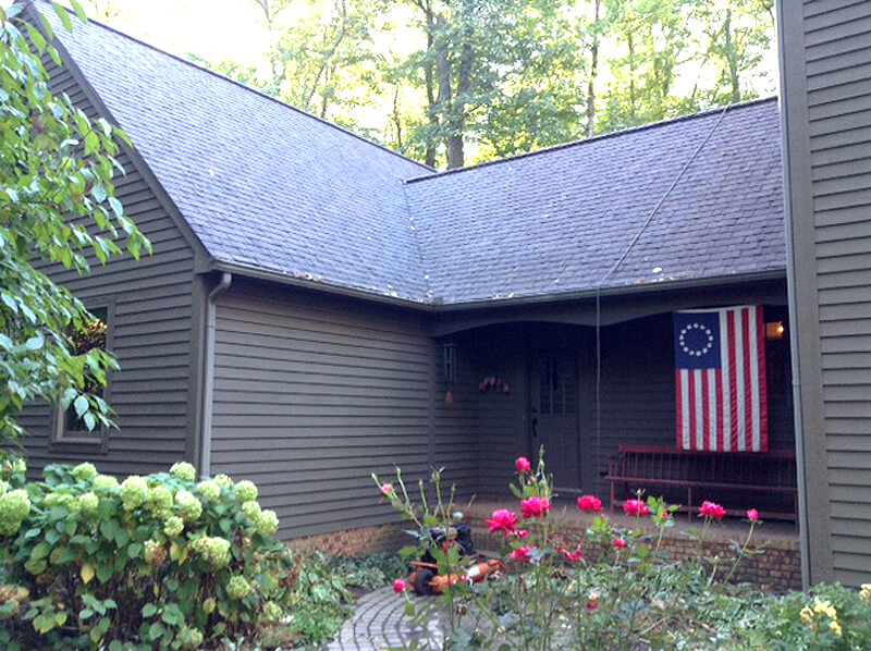 brown sided house with paver walkway, flowered landscaping and american flag hanging