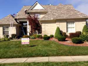 tan brick house with workers on top installing new roof