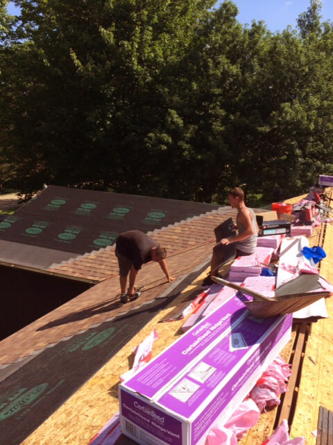 two men installing brown shingles on top of house roof
