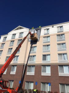 workers in cherry picker installing shingles on hotel roof