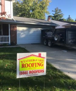 weatherguard roofing sign in front yard of older colonial-style house