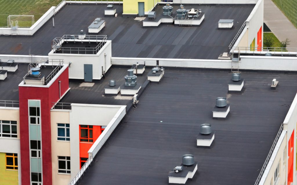 top view dark flat roof with air conditioners and hydro insulation membranes on top of a modern apartment building residential area.