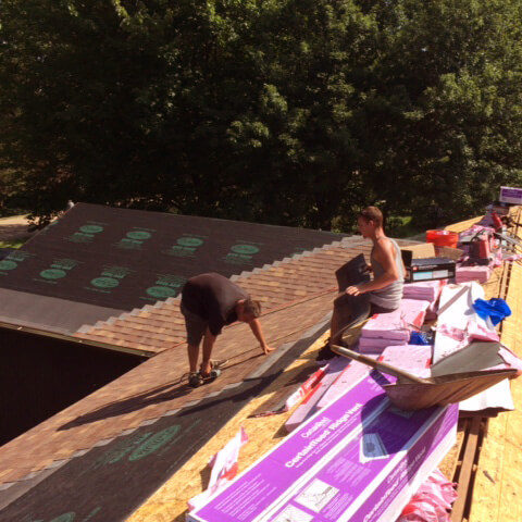 two men installing brown shingles on top of house roof